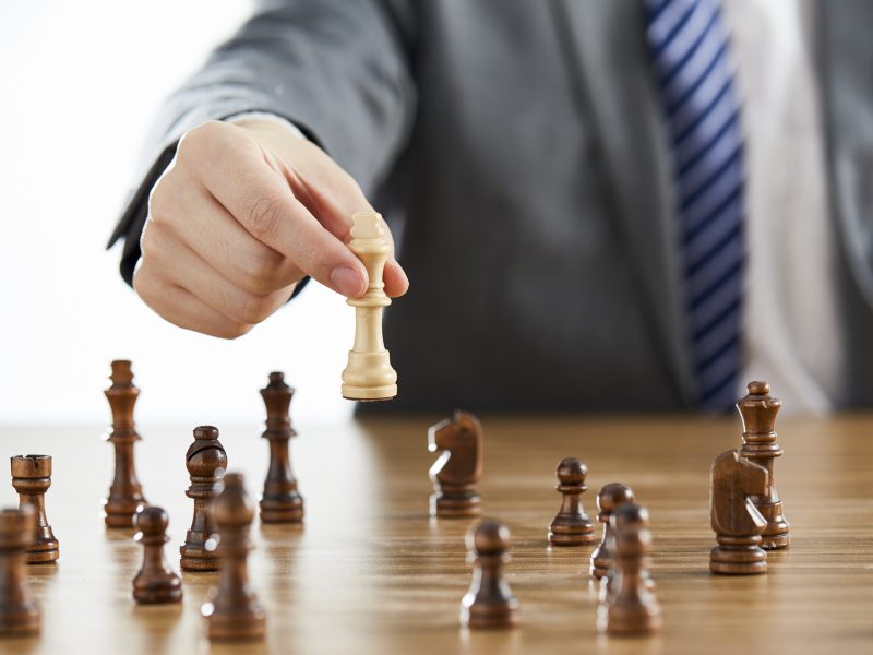 A businessman in a suit using his white king chess piece among dark chess pieces on a table - problem solving conce