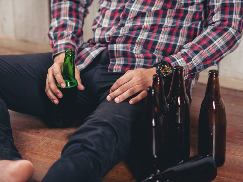 Alcohol addicted handsome man sitting alone with alcohol bottle