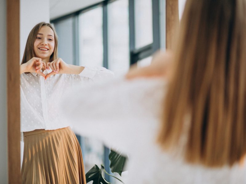 Pretty young woman in casual outfit looking into mirror